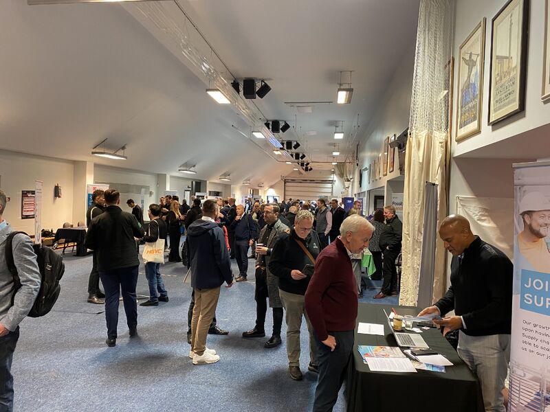 A busy indoor event space filled with attendees networking, browsing displays, and engaging at tables with informational materials at Marketplace Live.