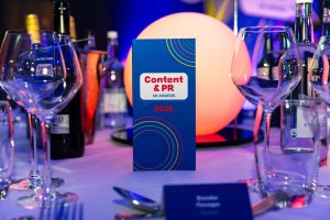 Table set for the 2025 Content & PR UK Awards, featuring a colourful menu, wine bottles, and elegant glassware.